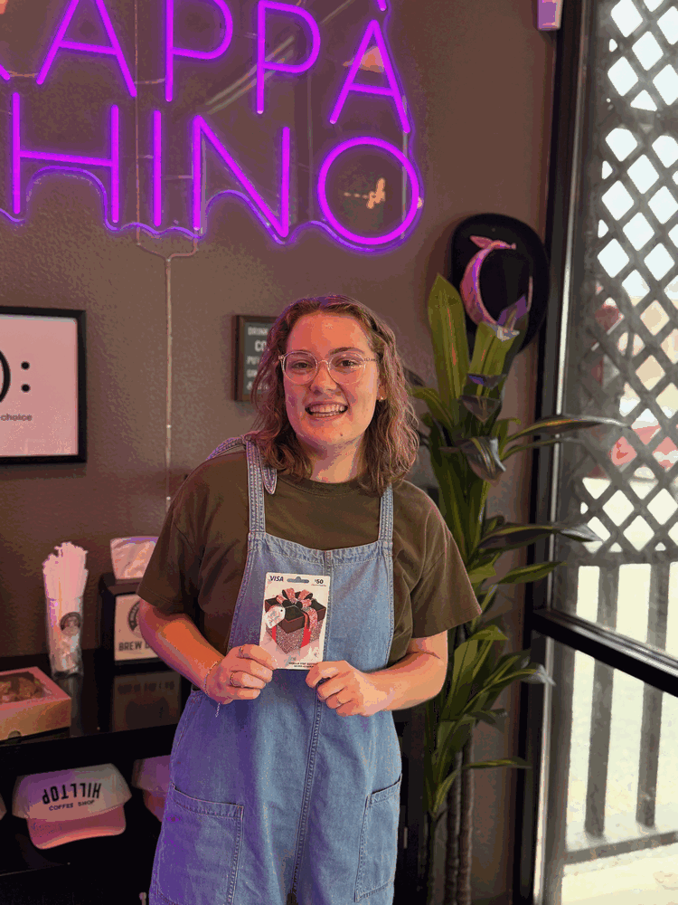 Hilltop Coffee Shop May Employee of the Month holding a $50 Visa gift card in front of the Frappakkhino neon sign